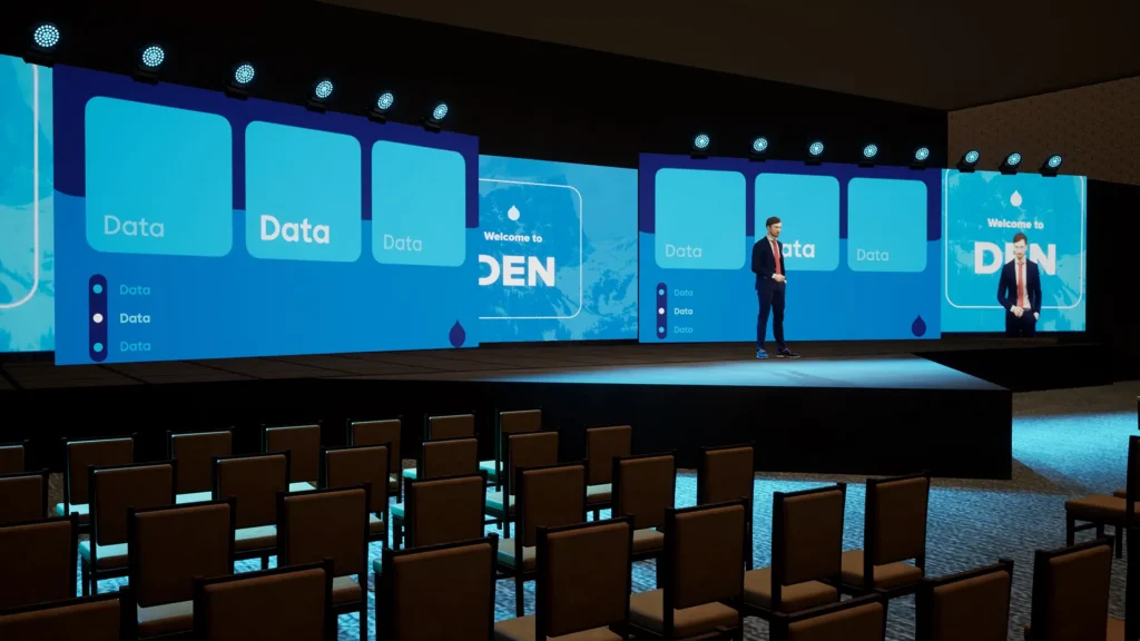 Wide conference stage setup with LED screens, presentation graphics, theatrical lighting, and a presenter during a live corporate event production.