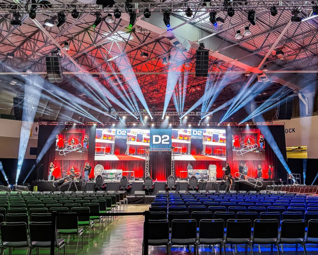 Encompass Event Group live event accessibility: rows of chairs face a red-lit stage with large screens, truss lighting, and suspended speakers.